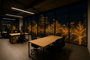 ガラス張りの広い無人オフィスから、クリスマスイルミネーションが輝く街の夜景を眺めるシーン。