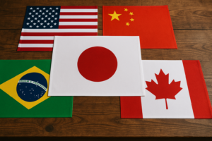 木製テーブルの上にアメリカ、中国、ブラジル、カナダの国旗が並び、中央に少し大きな日本の国旗が配置されたシーン