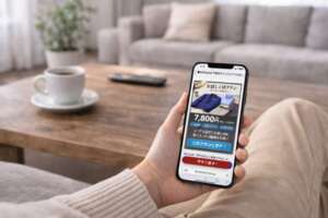 リビングのソファでくつろぎながら、スマートフォンでメンズファッションレンタルのお試し1回プラン（7,800円）を確認しているシーン